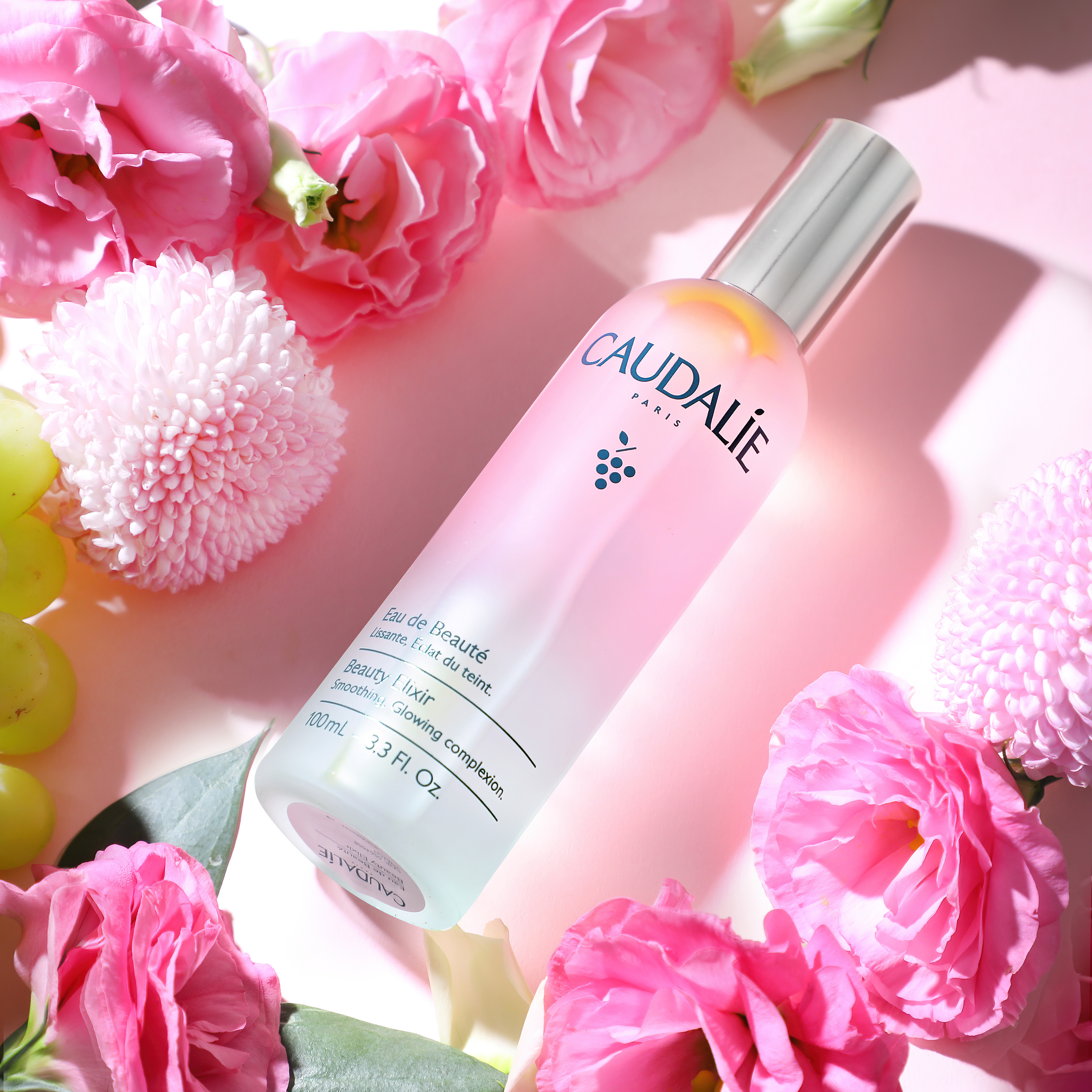 Editorial beauty product photography of Caudalie Beauty Elixir surrounded by fresh pink flowers with soft natural lighting. Premium skincare campaign photography by ProductPixels Singapore.