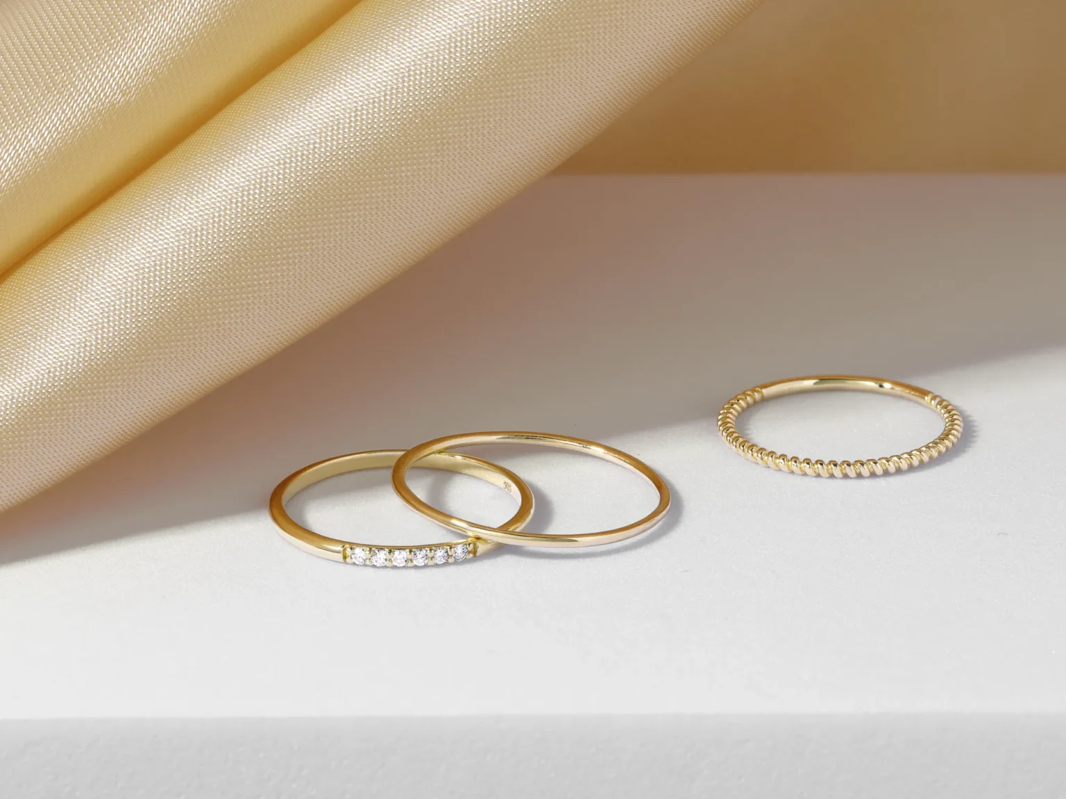 Delicate gold rings with a pav&eacute; diamond band on a soft neutral background photographed in Singapore.