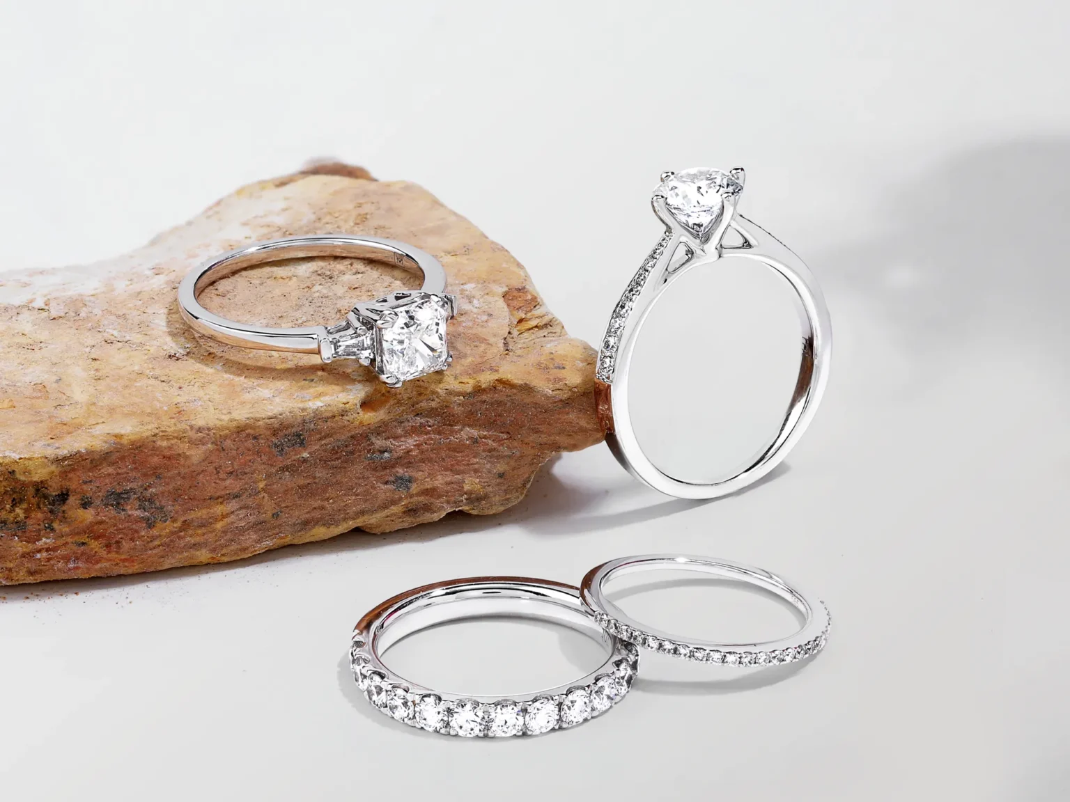 A collection of white gold diamond engagement rings and eternity bands styled on a raw natural stone and white background.