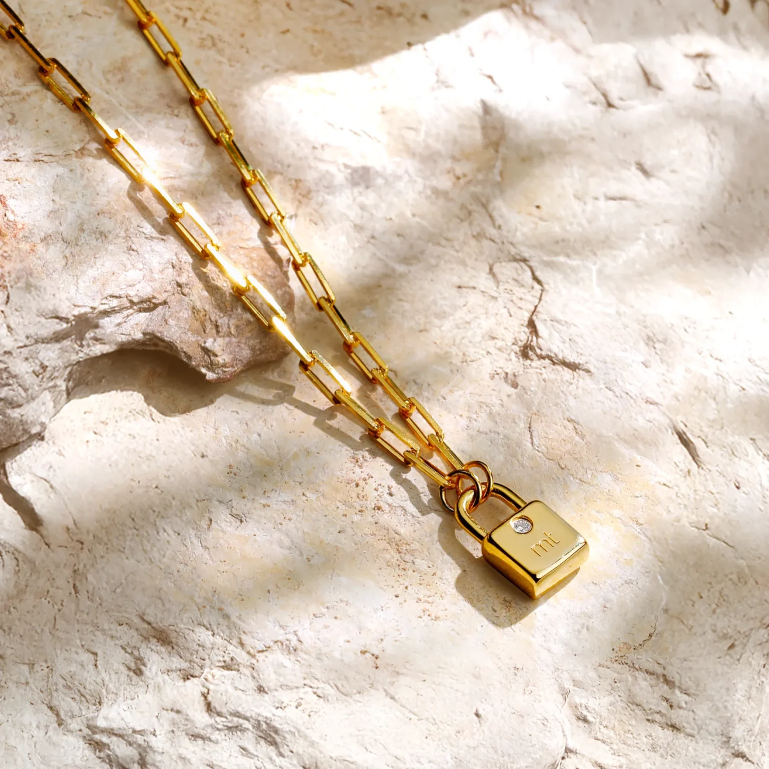 Personalized gold padlock pendant with diamond on a paperclip chain styled on raw limestone.