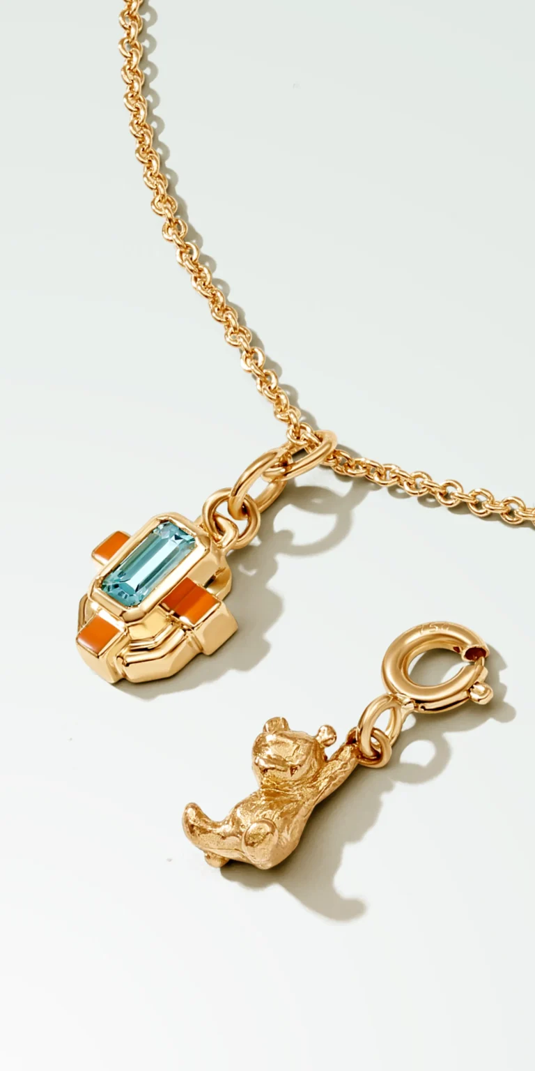 Gold pendant necklace with blue gemstone and charm detail on clean background, jewellery photography Singapore