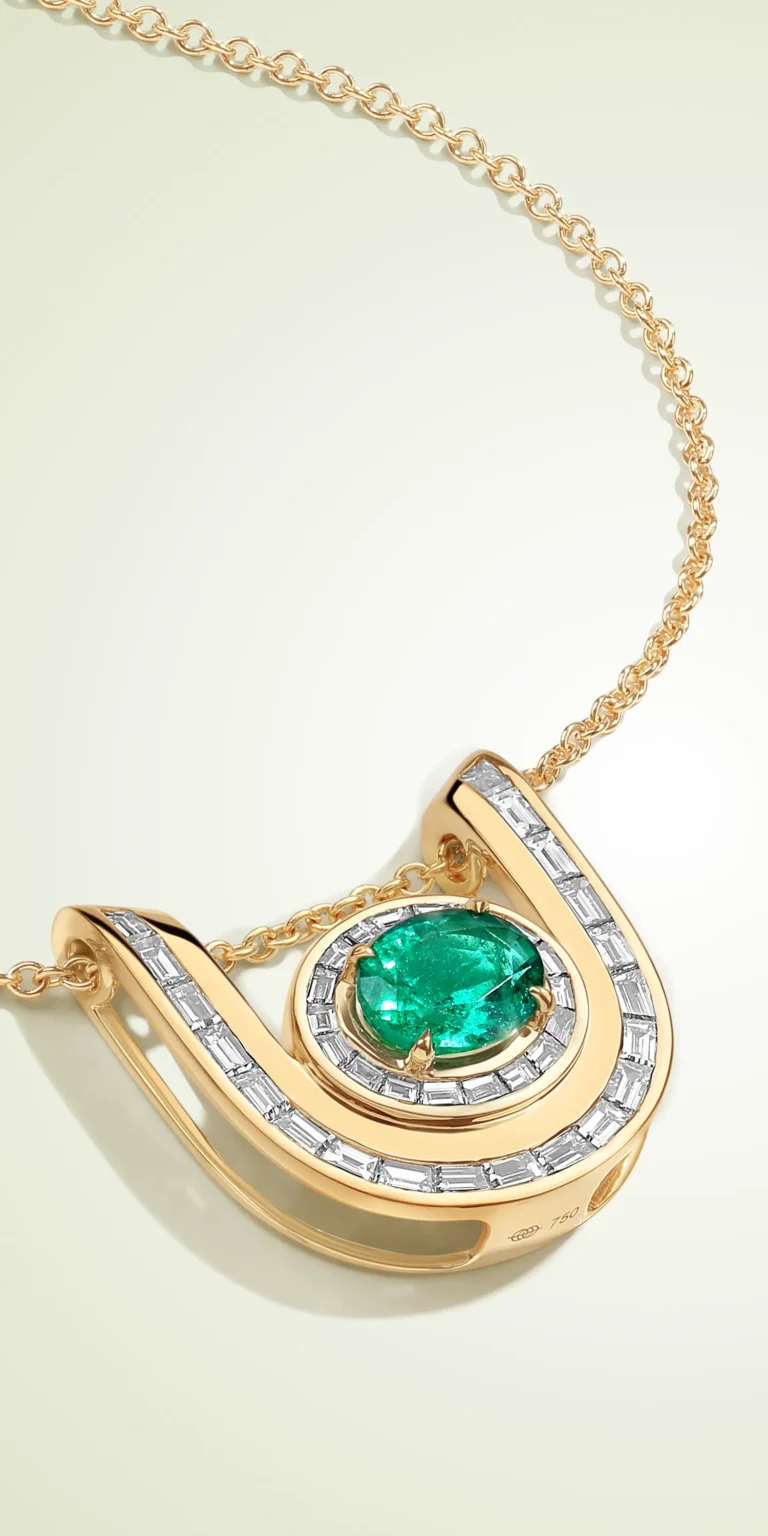 Gold pendant with green emerald and baguette diamond setting on clean background.