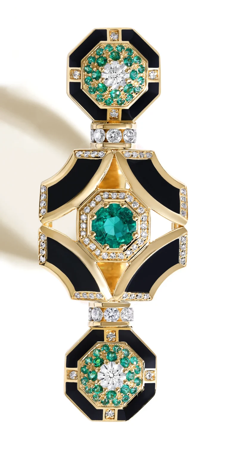 Gold jewellery piece with emeralds, diamonds and black enamel detailing on clean background.