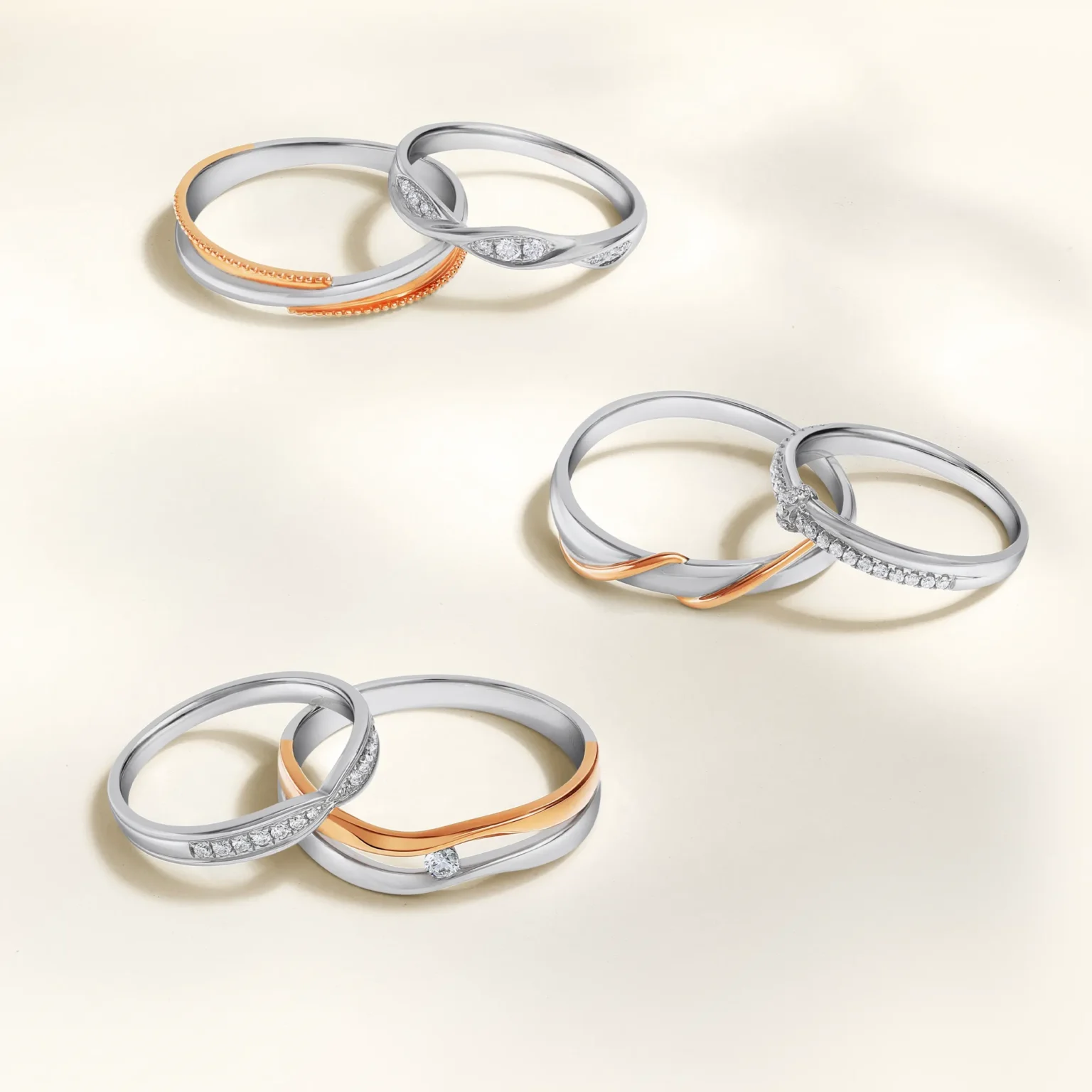 A commercial display of three pairs of interlocking wedding bands in platinum and rose gold, featuring wave-shaped silhouettes and pav&eacute; diamond accents.